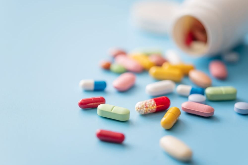 Colorful pills scattered from white plastic pill bottle on blue background.